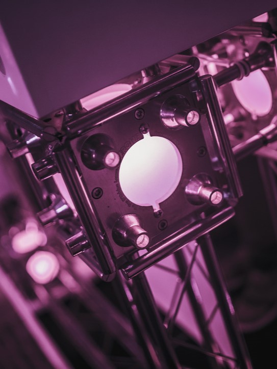 Metaal frame met cirkelvormige opening en vier draaiknoppen, verlicht met paars licht